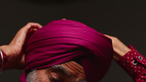 Primer-Plano,-Toma-De-Estudio-Con-Iluminación-Tenue-De-Un-Hombre-Sikh-Mayor-Con-Barba-Atando-Una-Tela-Para-Un-Turbante-Contra-Un-Fondo-Oscuro-2